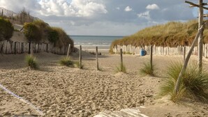 Een zandstrand met een houten omheining en een blauwe vaten.