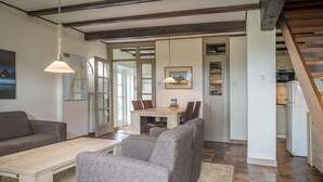 A modern living room with a sofa, a coffee table, and a dining area with chairs and a table. - Farmhouse in De Cocksdorp Near Beach (De Cocksdorp)