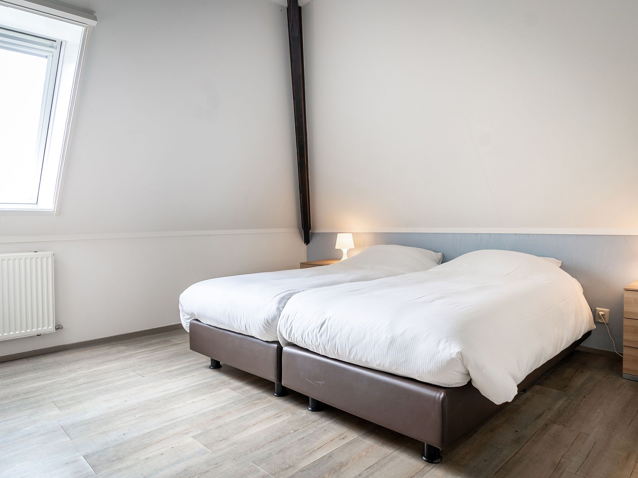 A bedroom with a bed, a nightstand, a lamp, and a window.