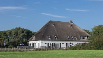 A large, white building with a steeply pitched roof, multiple windows, and a stone wall in front.