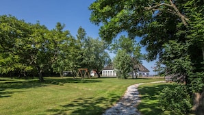 A grassy park with a gravel path, trees, and a swing set. - Farmhouse in De Cocksdorp Near Beach (De Cocksdorp)