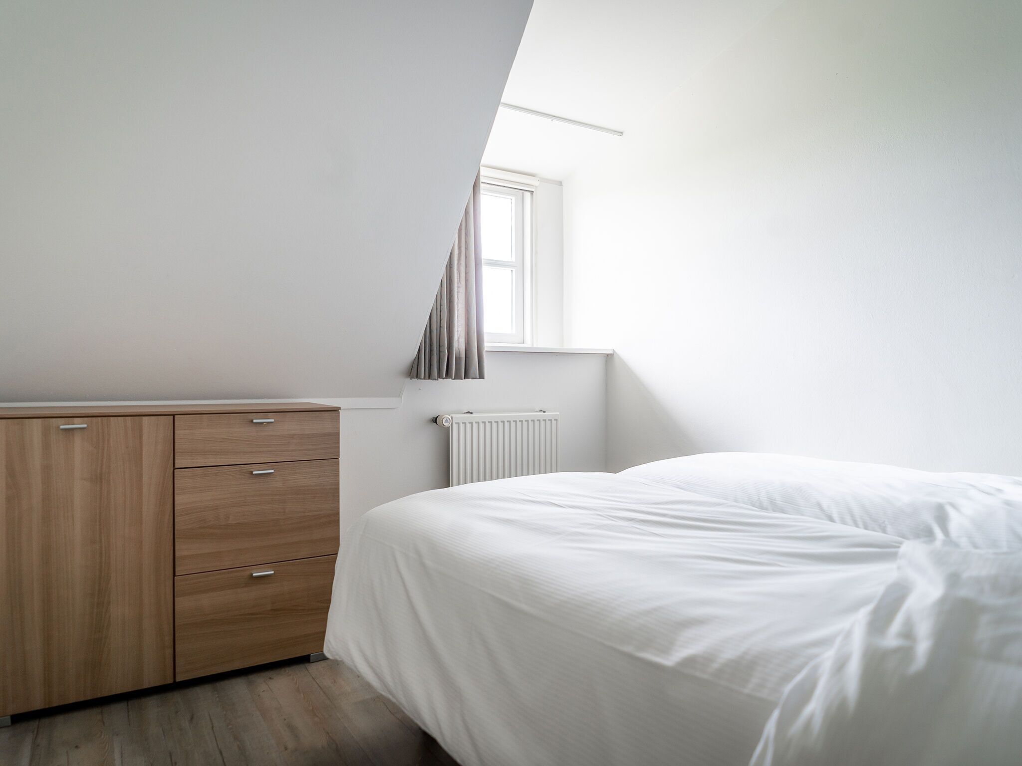 A bedroom with a bed, a wooden dresser, a window, and a radiator.