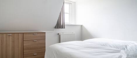 A bedroom with a bed, a wooden dresser, a window, and a radiator.