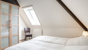 A bedroom with a sloped ceiling, a skylight, a radiator, a chair, and a bed. - Farmhouse in De Cocksdorp Near Beach (De Cocksdorp)