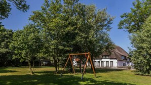 A grassy park area with a swing set and a white building with a dark roof in the background. - Farmhouse in De Cocksdorp Near Beach (De Cocksdorp)