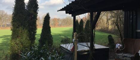 A covered patio area with a view of a green field and tall trees.