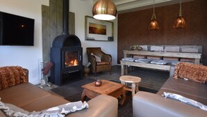 A cozy living room with a fireplace, comfortable seating, and a dining area with a wooden table and benches. - Alluring Holiday Home in Reutum-Weerselo with Hot Tub (Reutum)