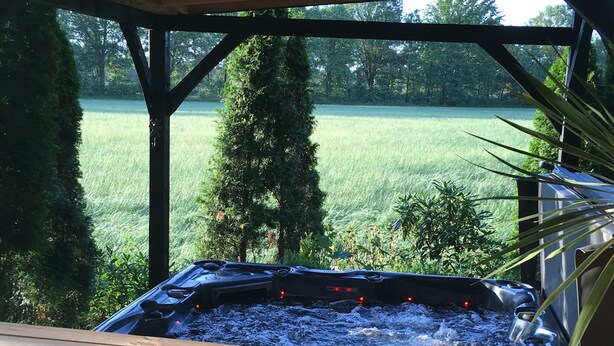 A hot tub with a wooden deck, surrounded by greenery and trees. - Alluring Holiday Home in Reutum-Weerselo with Hot Tub (Reutum)