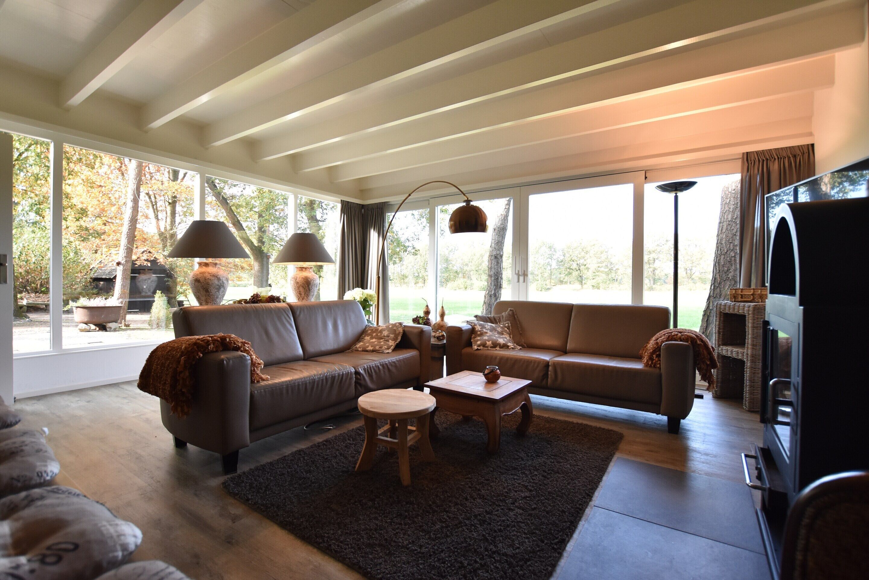 Una sala de estar moderna con dos sofás, una mesa de centro y un televisor. Amplias ventanas ofrecen vistas al exterior.