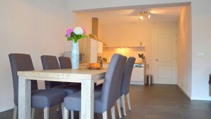 Un comedor con una mesa de madera y seis sillas, un jarrón con flores y una cocina al fondo.