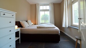 Un dormitorio con cama, mesita de noche, cómoda y ventana con cortinas.