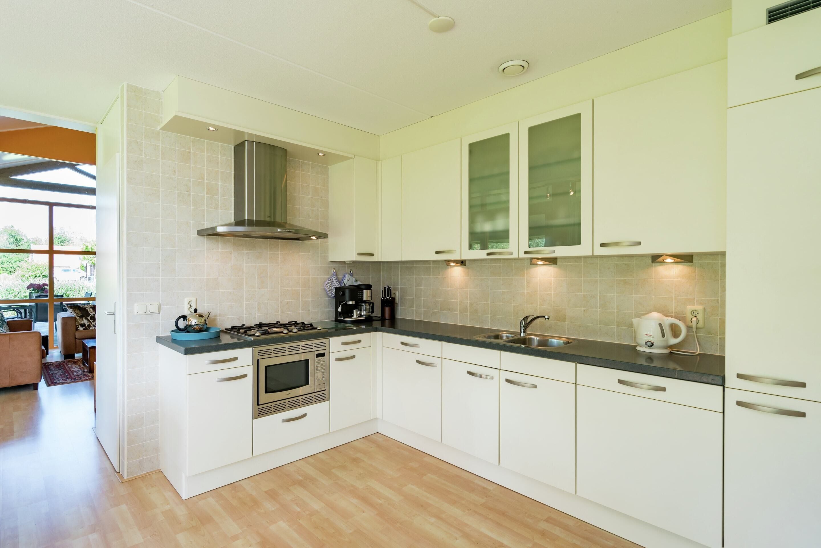A modern kitchen with white cabinets, a stainless steel range hood, a built-in oven, and a large window providing natural light.