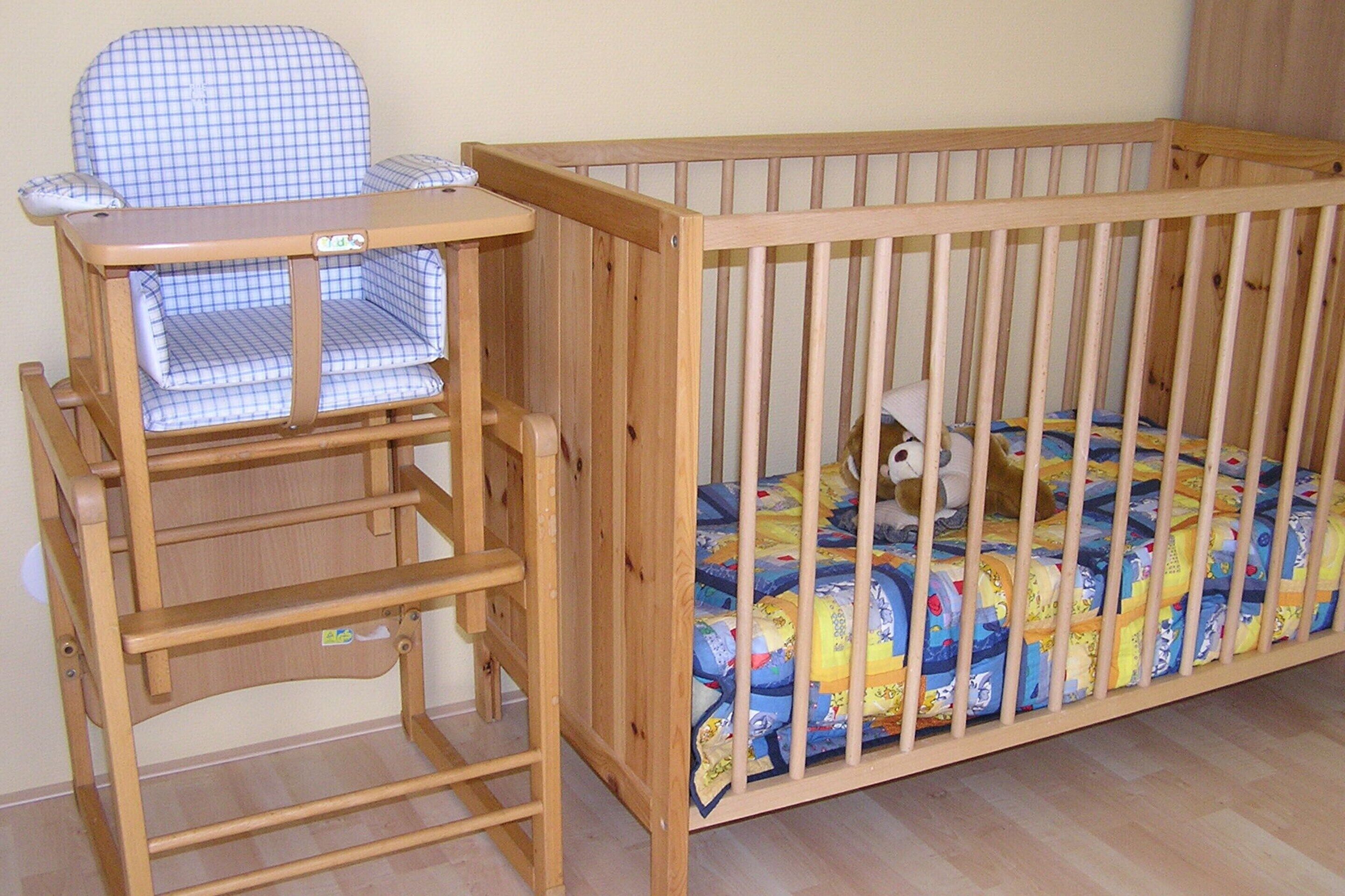 Ein hölzernes Babybett mit integrierter Wickelkommode, eine gemusterte Bettdecke und ein Holzboden.