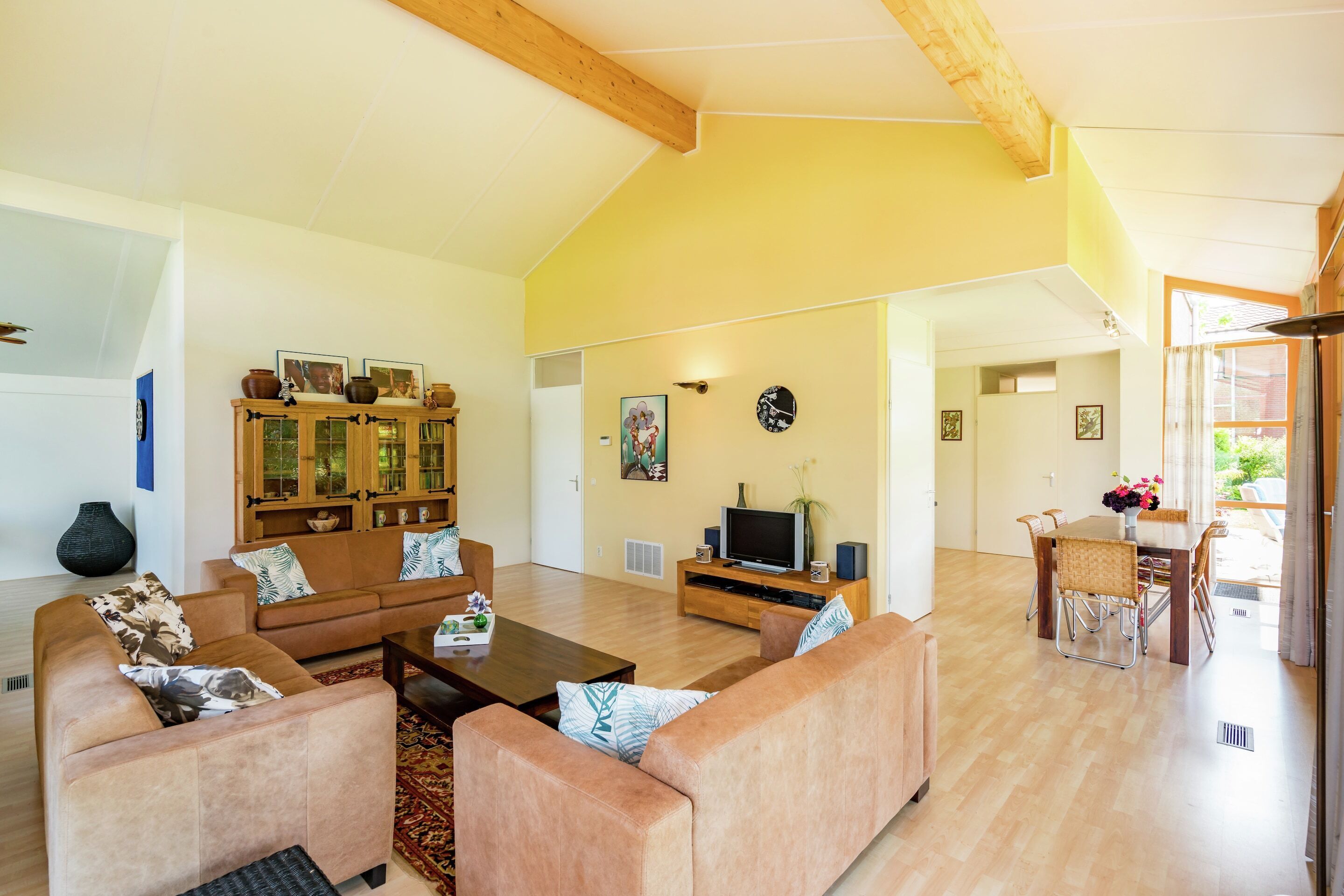Una sala de estar amplia con techo alto, una mesa de comedor de madera con sillas, un conjunto de sofás y un televisor sobre un mueble de madera.