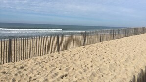 Una playa arenosa con una valla de madera y olas del océano.