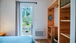Un dormitorio con una cama, una puerta que da a un balcón, un estante pequeño y un respiradero instalado en la pared.
