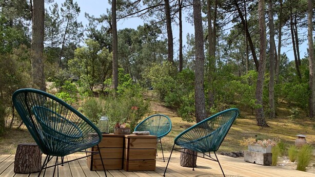 Una terraza de madera con tres sillas de estructura metálica verde y una mesa de madera.