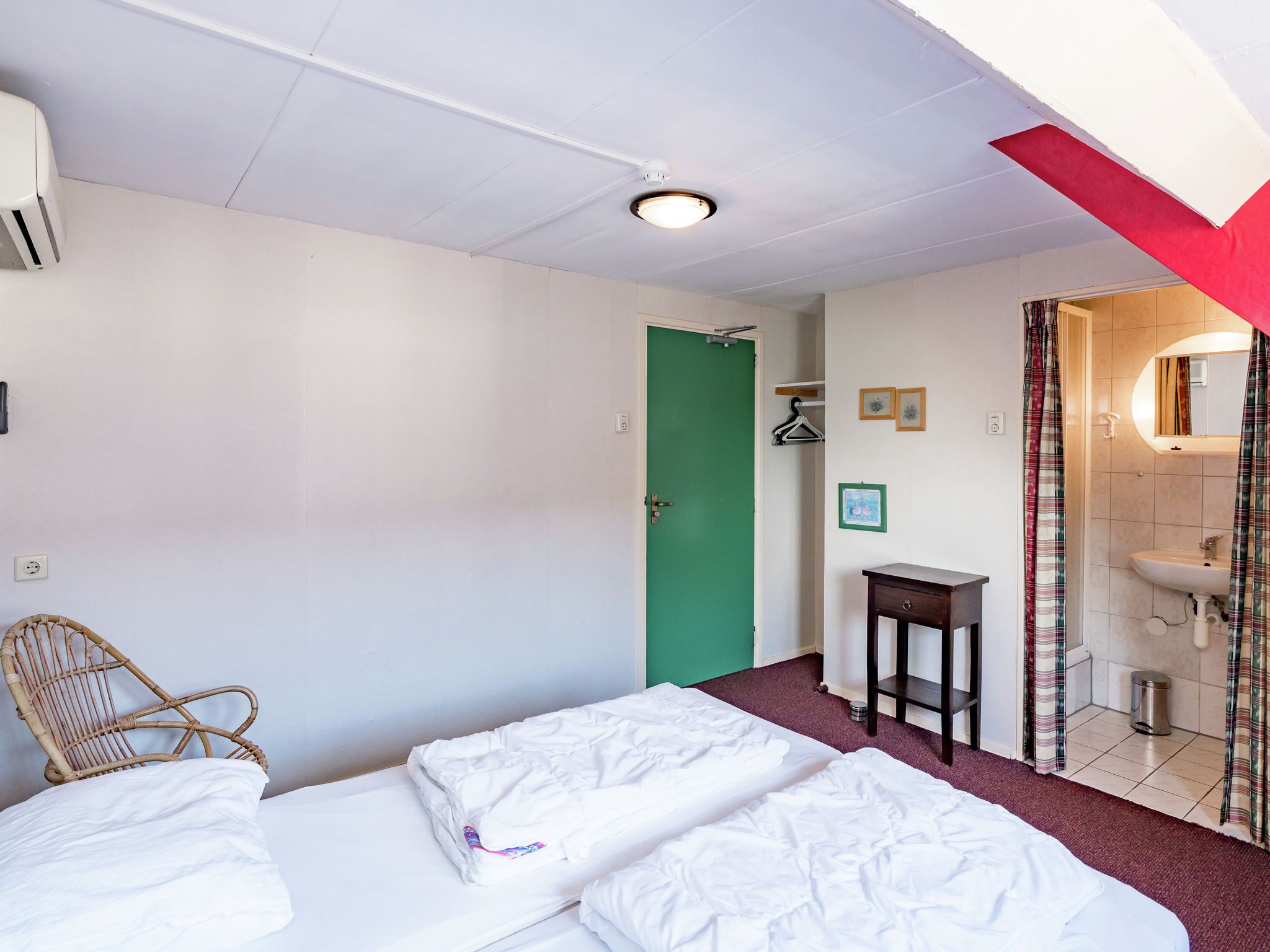 Une chambre d’hôtel avec un lit, une chaise, une petite table, une salle de bain avec un lavabo et une porte verte.