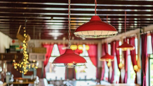 Interno di un ristorante con lampade a sospensione rosse, tavoli in legno e un divano blu.