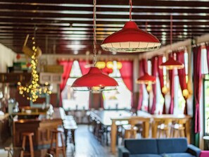 A restaurant interior with hanging red pendant lights, wooden tables, and a blue sofa. - Quaint Holiday Home in Friesland by the Lake (Scherpenzeel)