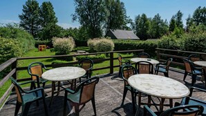 Patio esterno con tavoli e sedie rotonde, circondato da un muretto e una recinzione in legno.