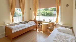 Una stanza con un letto, un tavolino e una sedia. Alle finestre sono presenti delle tende.