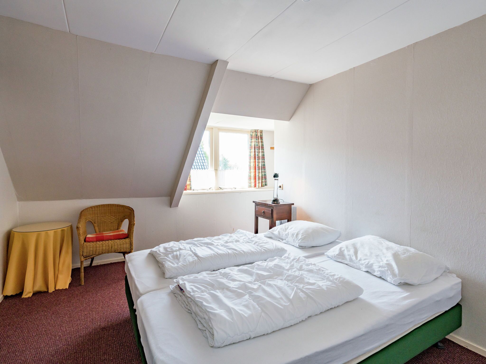 A bedroom with two beds, a window with curtains, a chair, and a small table.