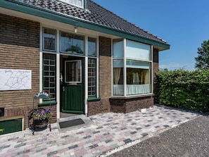 Ein Backsteinhaus mit grüner Tür, großen Fenstern und einem Willkommensschild.