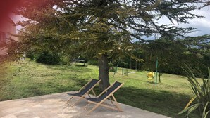 A patio area with two lounge chairs, a grassy lawn, and a playground in the background. - Holiday Home Provence With Pool (Cereste)