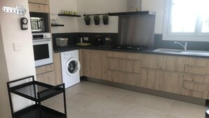 A modern kitchen with a washing machine, oven, and stove. There is a black chair and a shelf with plants. - Holiday Home Provence With Pool (Cereste)