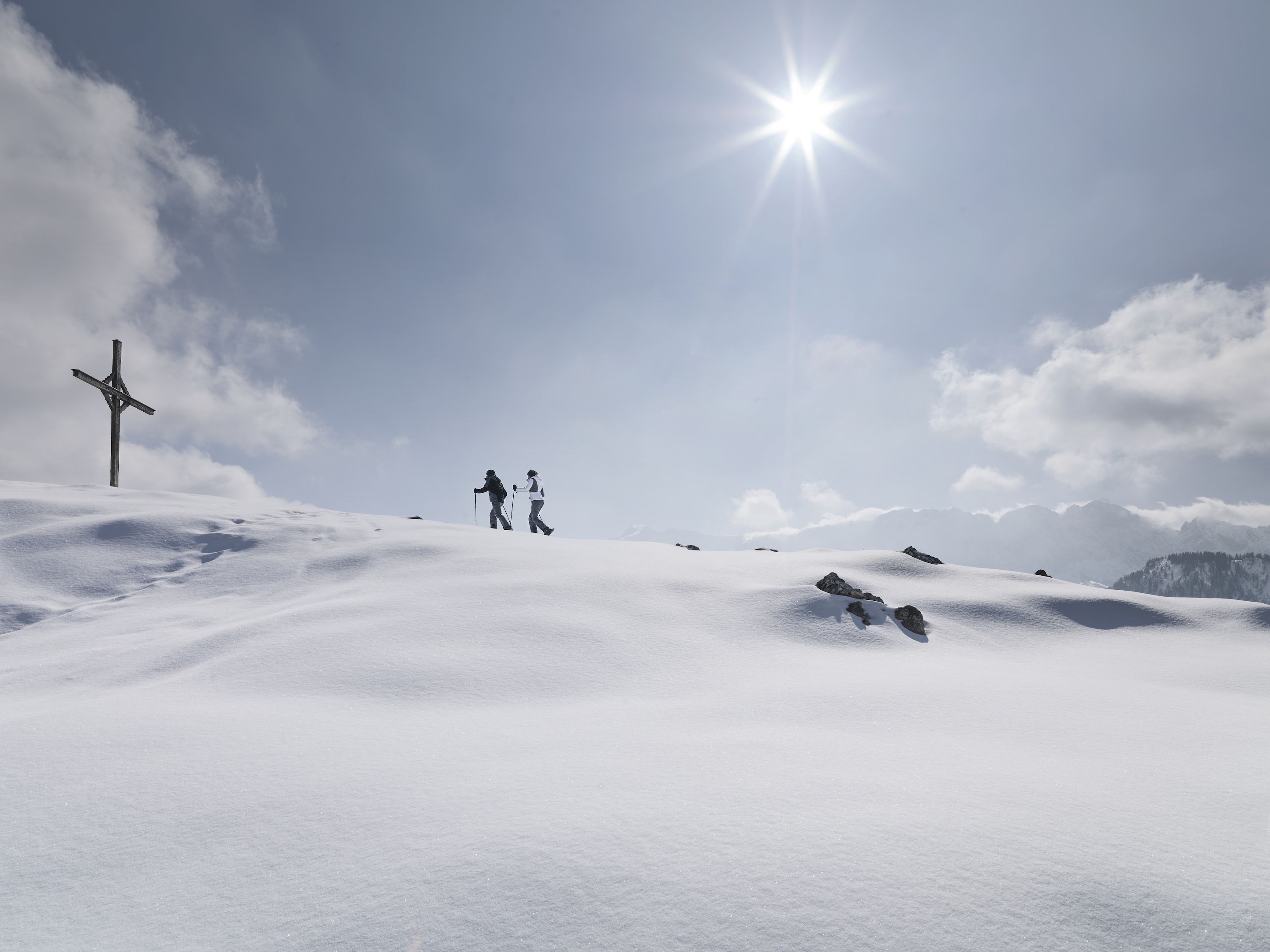 Schneeverdeckte Landschaft mit einem hölzernen Kreuz und zwei Wanderern.