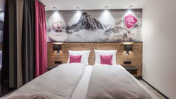 Une chambre d’hôtel avec un lit, deux tables de chevet, une lampe fixée au mur et une grande affiche représentant une montagne.
