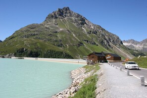 Un chalet de montagne à l’extérieur en bois, situé le long d’une route goudronnée, et surplombant un lac d’un bleu limpide.