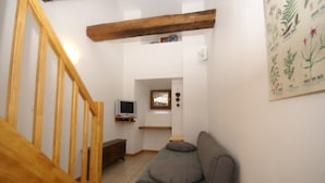 Een trap met houten leuningen, een grijze bank met kussens, een televisie op een standaard en een wandplank met decoratieve objecten.