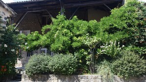 Een stenen gebouw met een rustiek dak, omgeven door weelderige begroeiing en bloeiende planten.