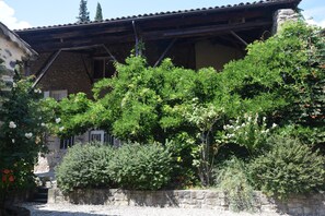A stone building with a rustic roof, surrounded by lush greenery and flowering plants. - Holiday Home in Ardeche With Pool & Garden (Lalevade-d'Ardeche)