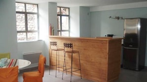 Een keuken met een houten kookeiland, twee barkrukken, een koelkast en een raam met uitzicht op een stenen muur.