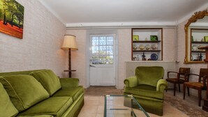 A living room with a green sofa, a green armchair, a glass coffee table, a lamp, a door with a window, and shelves with decorative items. - Vintage Retreat in Montfaucon (Montfaucon)