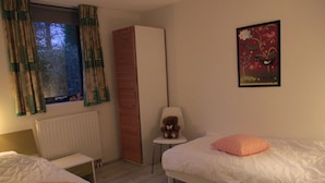 Ein Schlafzimmer mit zwei Betten, einem Heizkörper, einem Fenster mit Vorhängen, einem Sessel, einem Teddybären und einem Poster an der Wand.