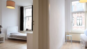 Una camera da letto con un letto, un comodino, una lampada, una finestra e un termosifone.