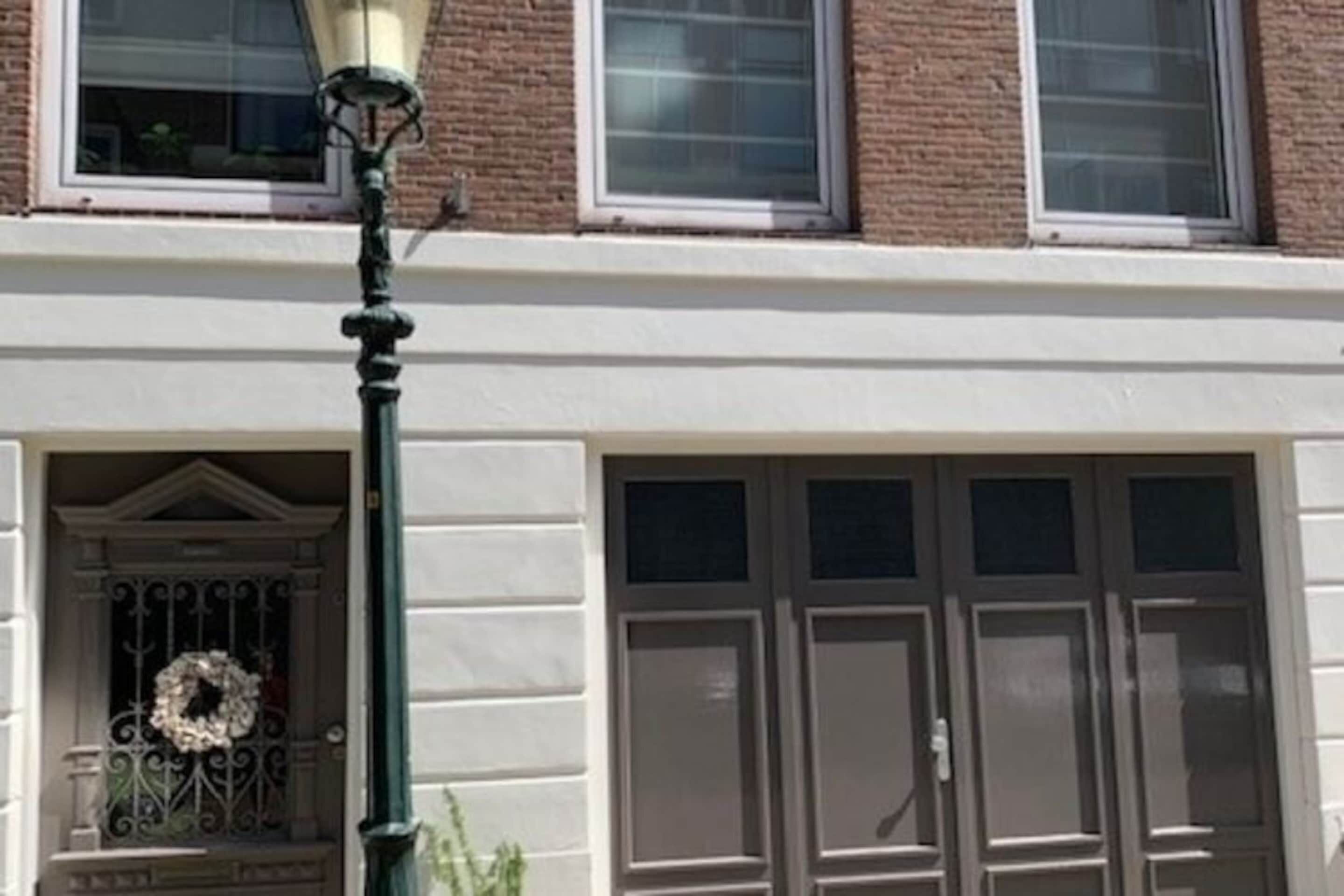Fachada de edificio con un ventanal grande y simétrico, un adorno de guirnalda en la puerta y una farola.