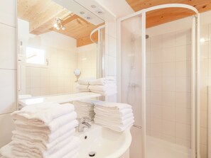 Une salle de bain moderne avec un plafond en bois, un lavabo surmonté d’une pile de serviettes, une douche en verre et un miroir.