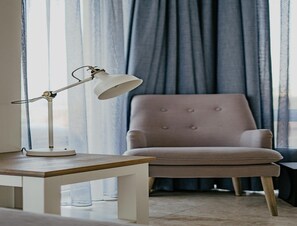 A room with a wooden table, a white lamp, and a tufted armchair. - Luxury Apartment Near the North Sea (Egmond aan Zee)