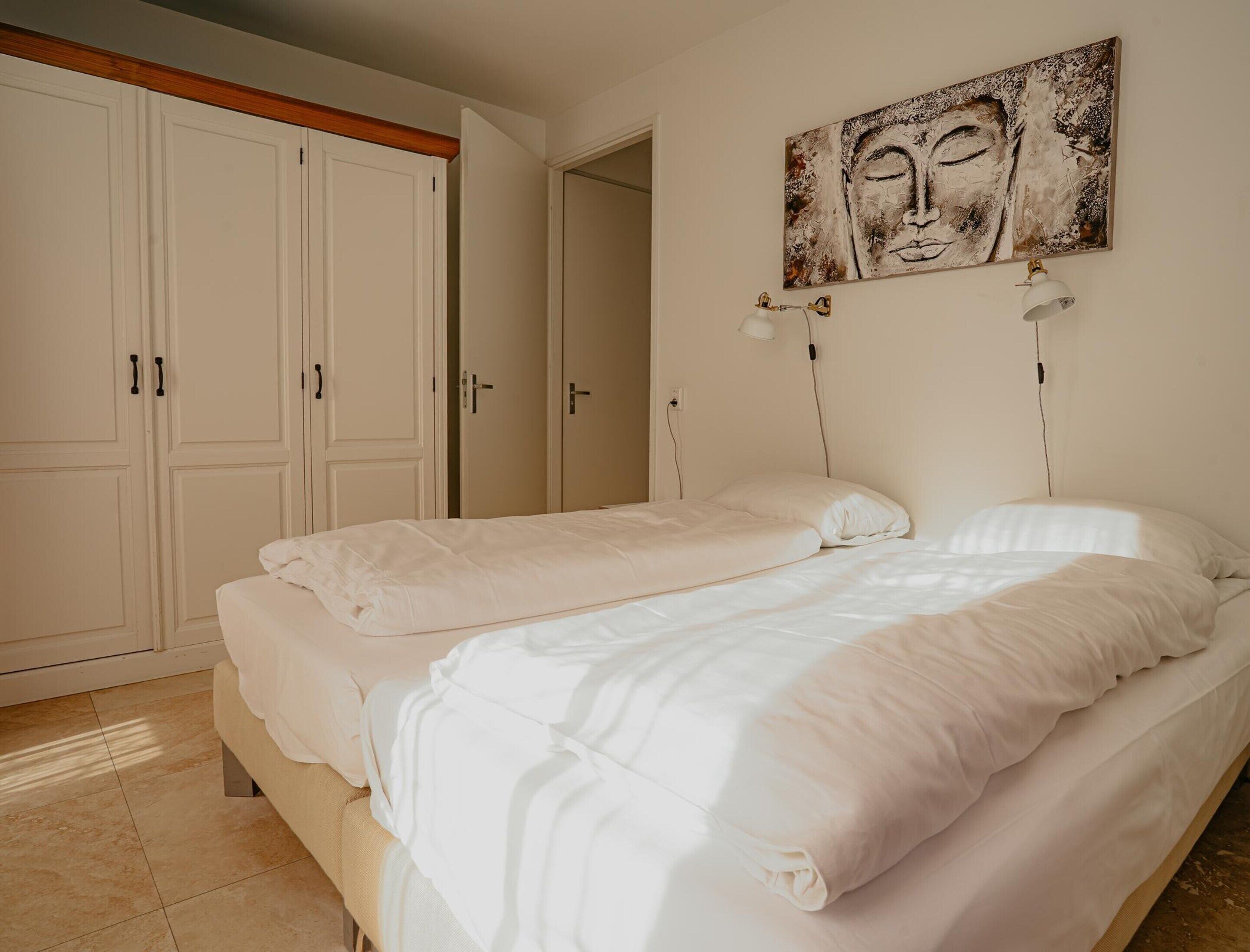 A bedroom with two beds, a large wardrobe, and a painting on the wall.