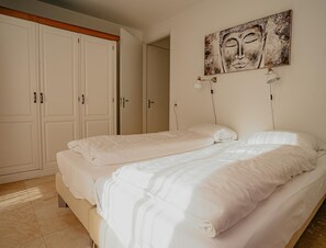 A bedroom with two beds, a large wardrobe, and a painting on the wall. - Luxury Apartment Near the North Sea (Egmond aan Zee)