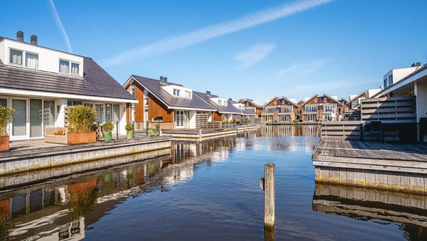 Een woongebied aan een gracht met huizen, houten looppaden en een rustig wateroppervlak dat de gebouwen weerspiegelt.