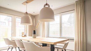 A modern dining room with a wooden table, white chairs, and pendant lights. - Spacious Bungalow in the Cosy Village (De Cocksdorp)