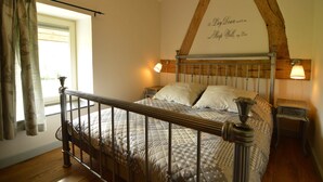 A bedroom with a wooden bed frame, a window with curtains, a wall-mounted light, and a decorative wall piece.
