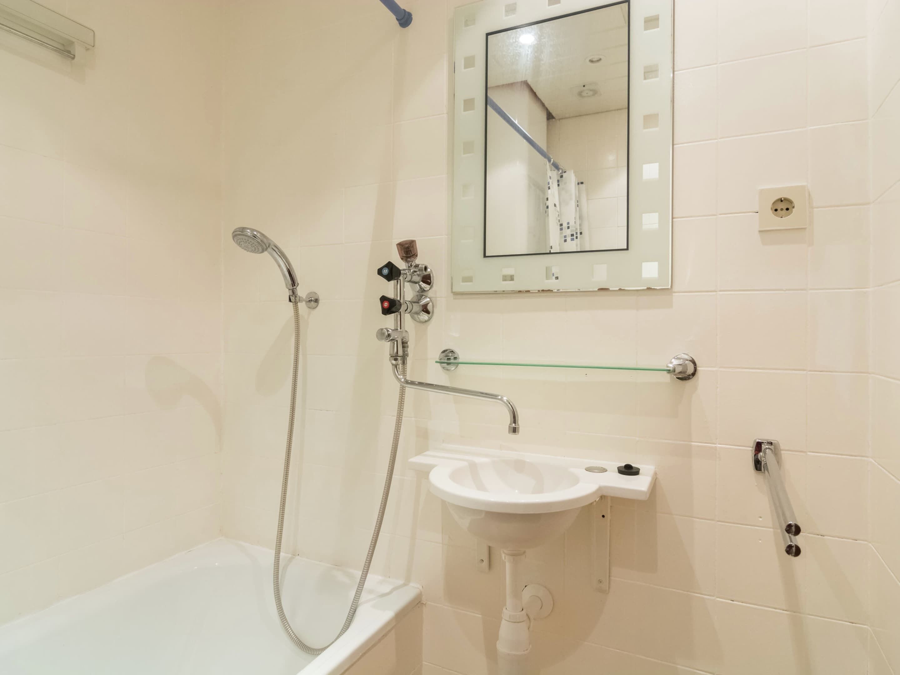 A bathroom with a bathtub, a sink, a shower with a handheld showerhead, and a mirror with a reflection of the bathroom.