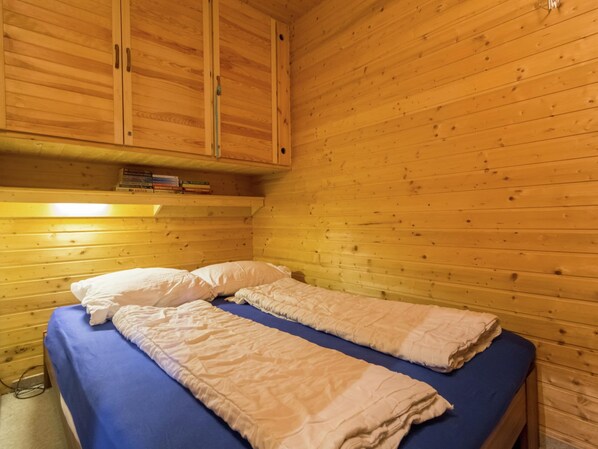A wooden cabin room with a bed, a shelf with books, and a wooden ceiling. - Apartment in Tauplitz Near Ski Lift (Bad Mitterndorf)